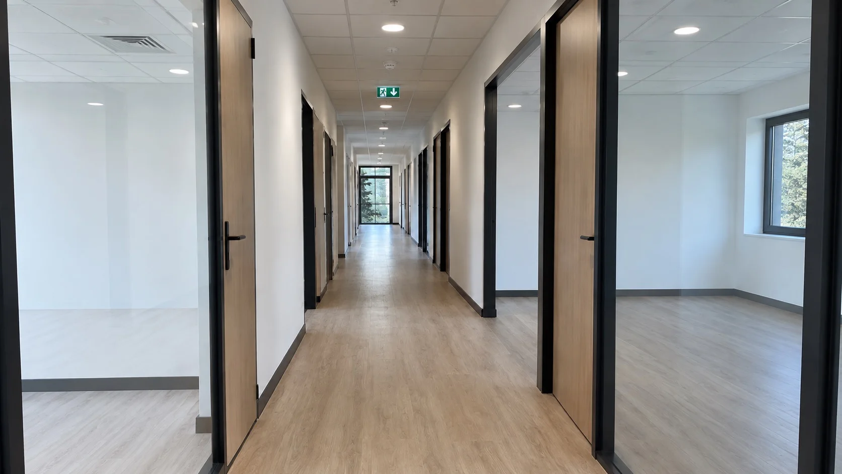 Couloir de bureaux desservant des espaces séparés par des cloisons vitrées à châssis noirs, portes bois clair et sol stratifié, ECM à Vienne, Bourgoin-Jallieu et Lyon